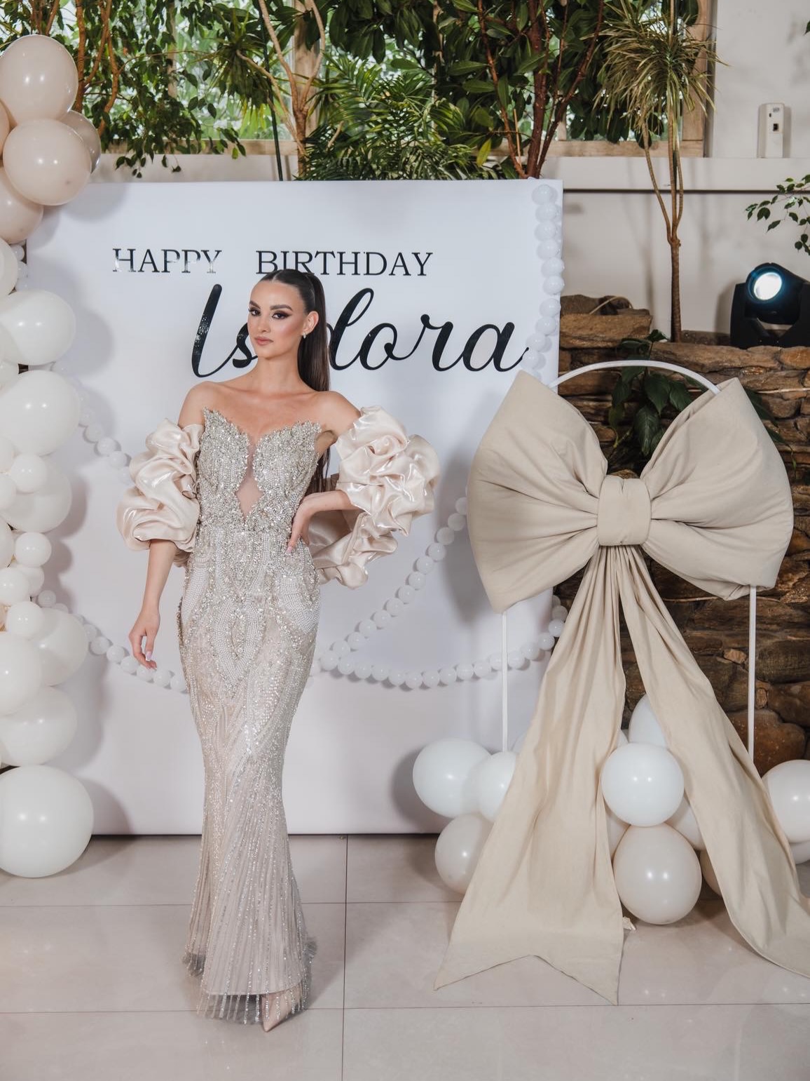 Elegantna bela foto-zona za rođendansku proslavu sa personalizovanom pozadinom, balonima i mašnom