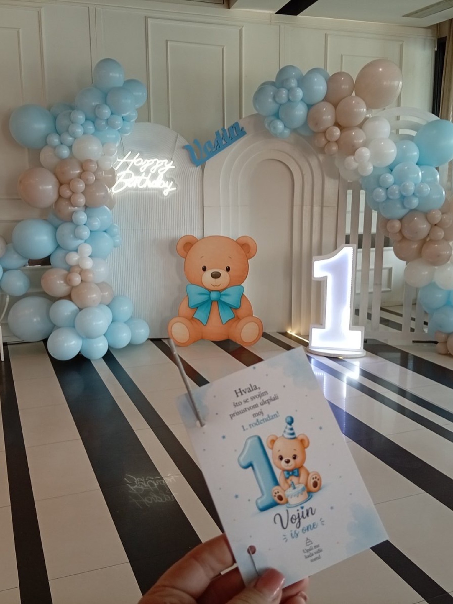Plavo-bela dekoracija prvog rođendana u Groš Plaza Event Centru sa medom, balonskim lukom i svetlećim brojem jedan